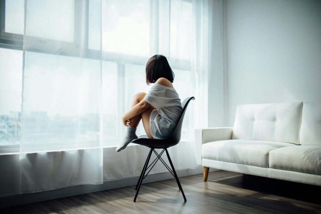 Girl sitting on chair looking out of the window, feeling sad